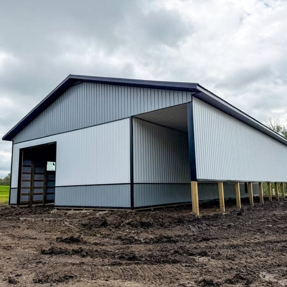 Completed post frame building with white metal siding and open bay under a cloudy sky