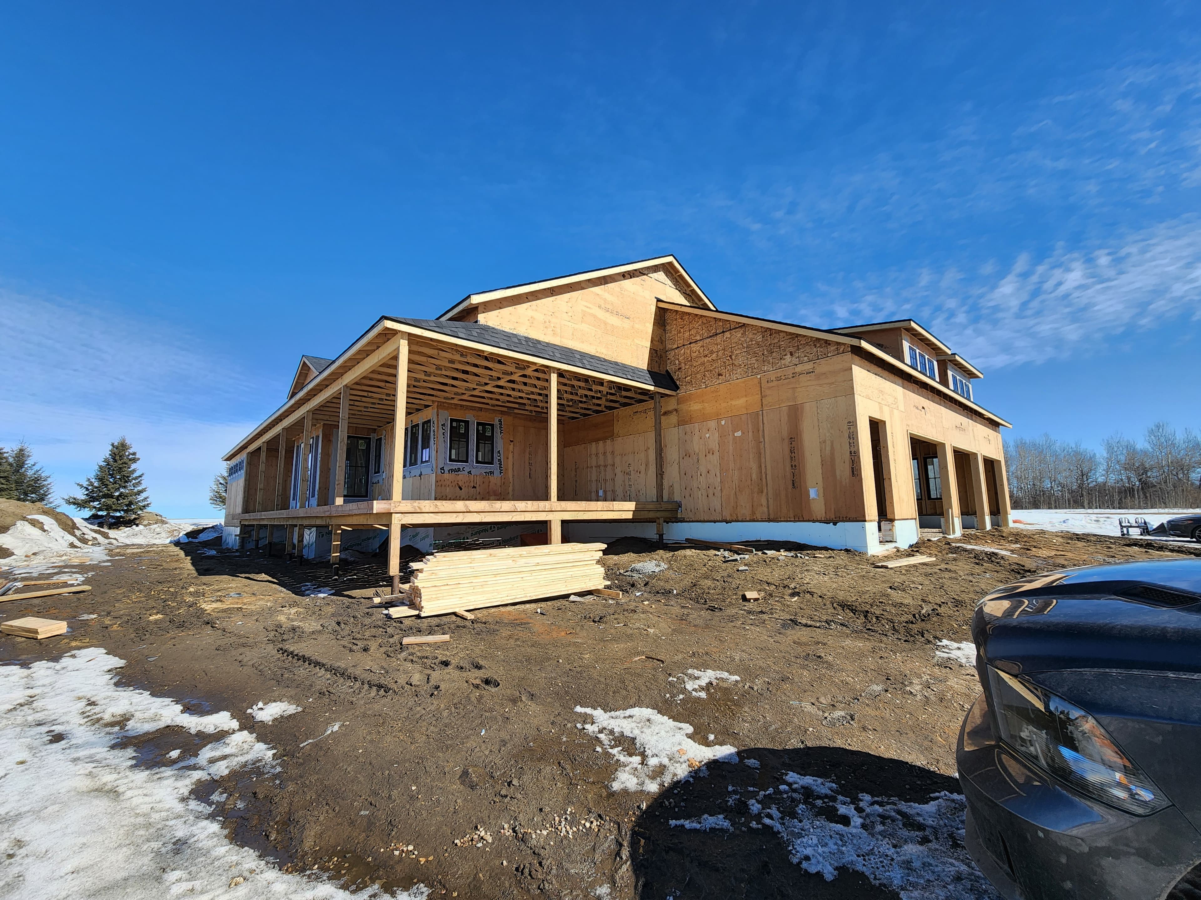 Residential home under construction with covered front porch and sheathed exterior walls in winter