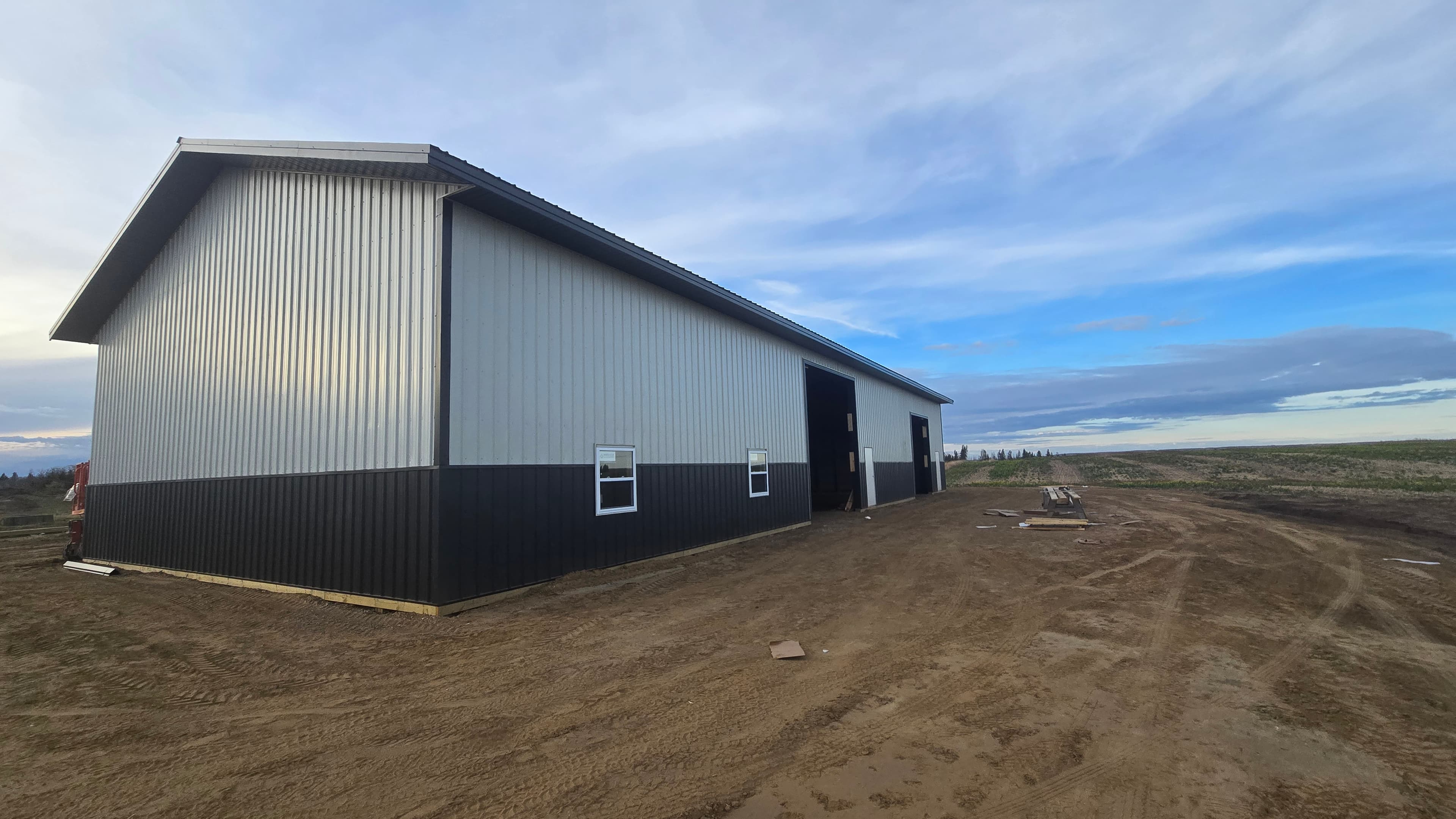 Completed two-tone post frame building with white upper siding, dark trim, and open bay doors