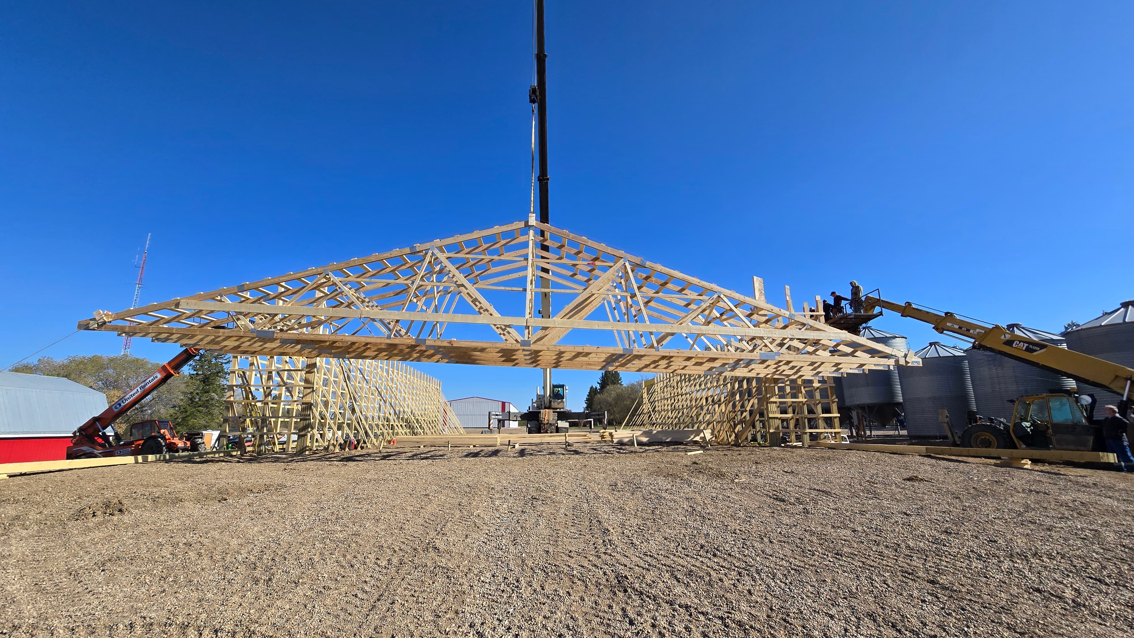 Crane lifting a large post frame roof truss into place with crew working from an aerial lift